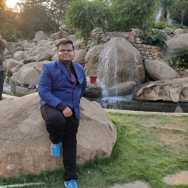 Aditya sitting on a boulder by a small waterfall at golden hour
